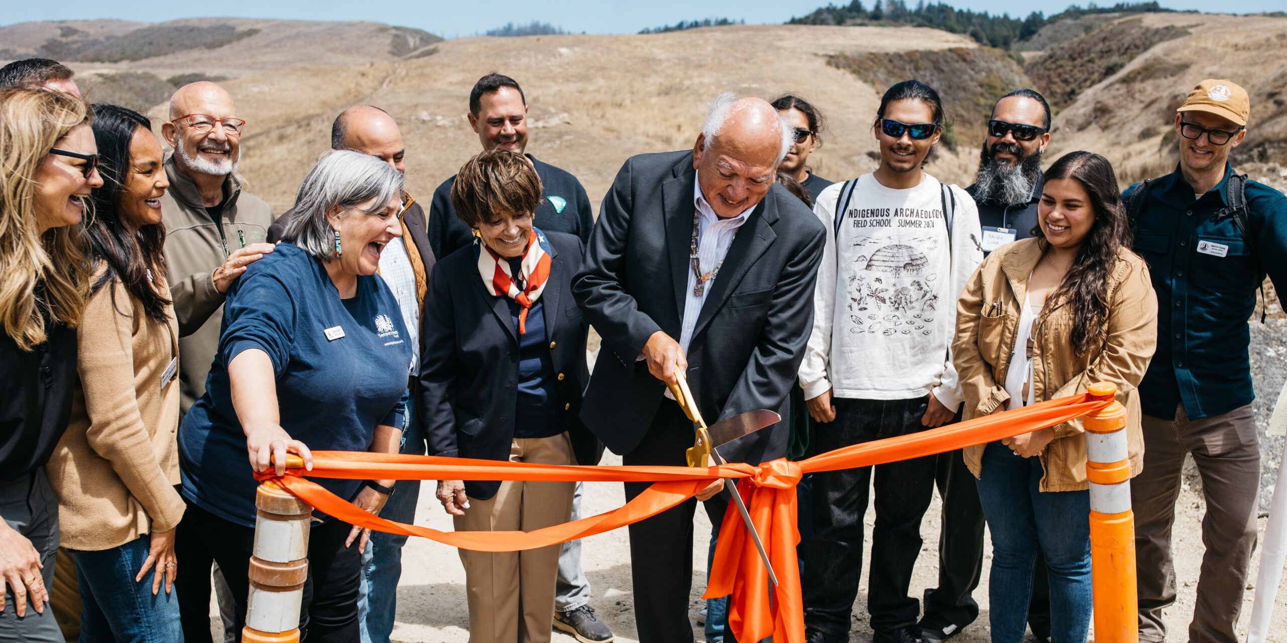 A diverse group of people cut a ribbon in front of newly opened public lands