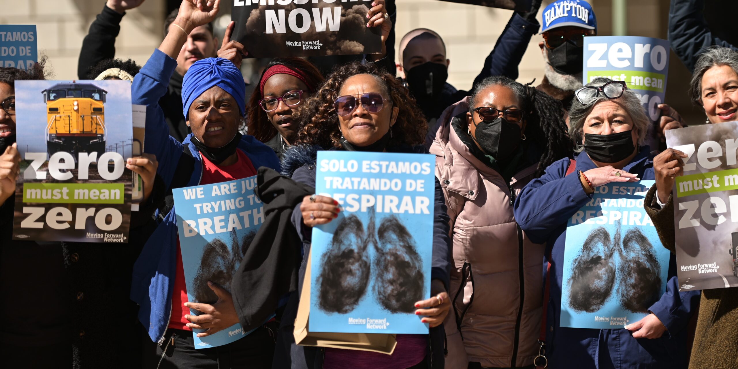 A racially diverse group of people hold signs calling for Zero Emissions Now