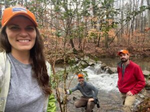 Three people standing on the bank of a river