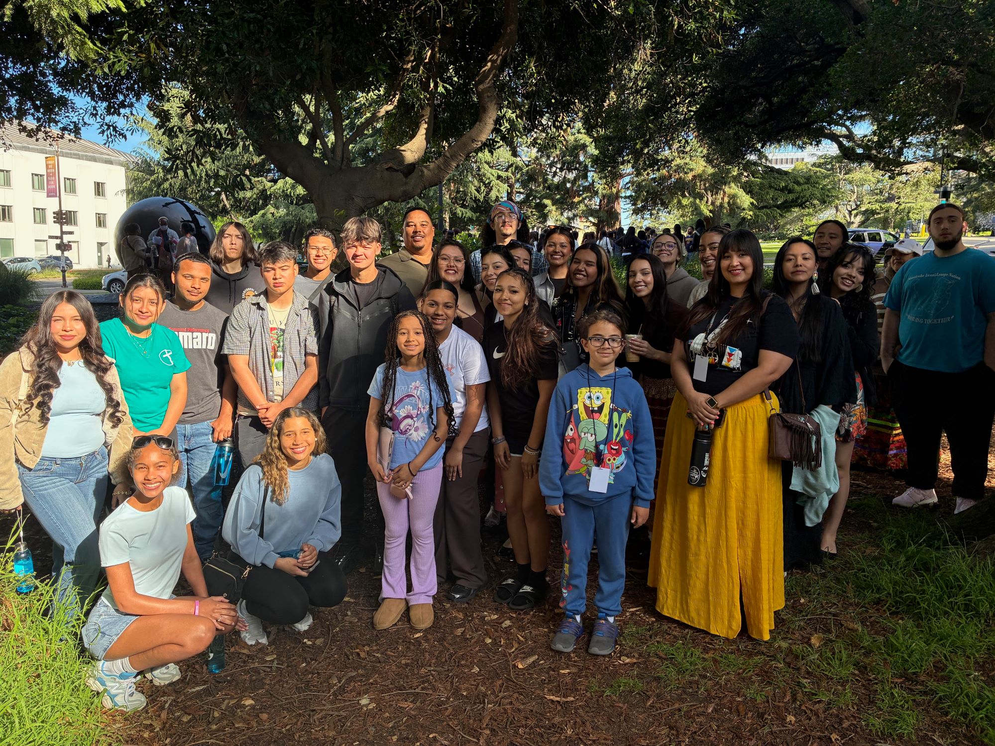 A group of Indigenous youth standing together under trees